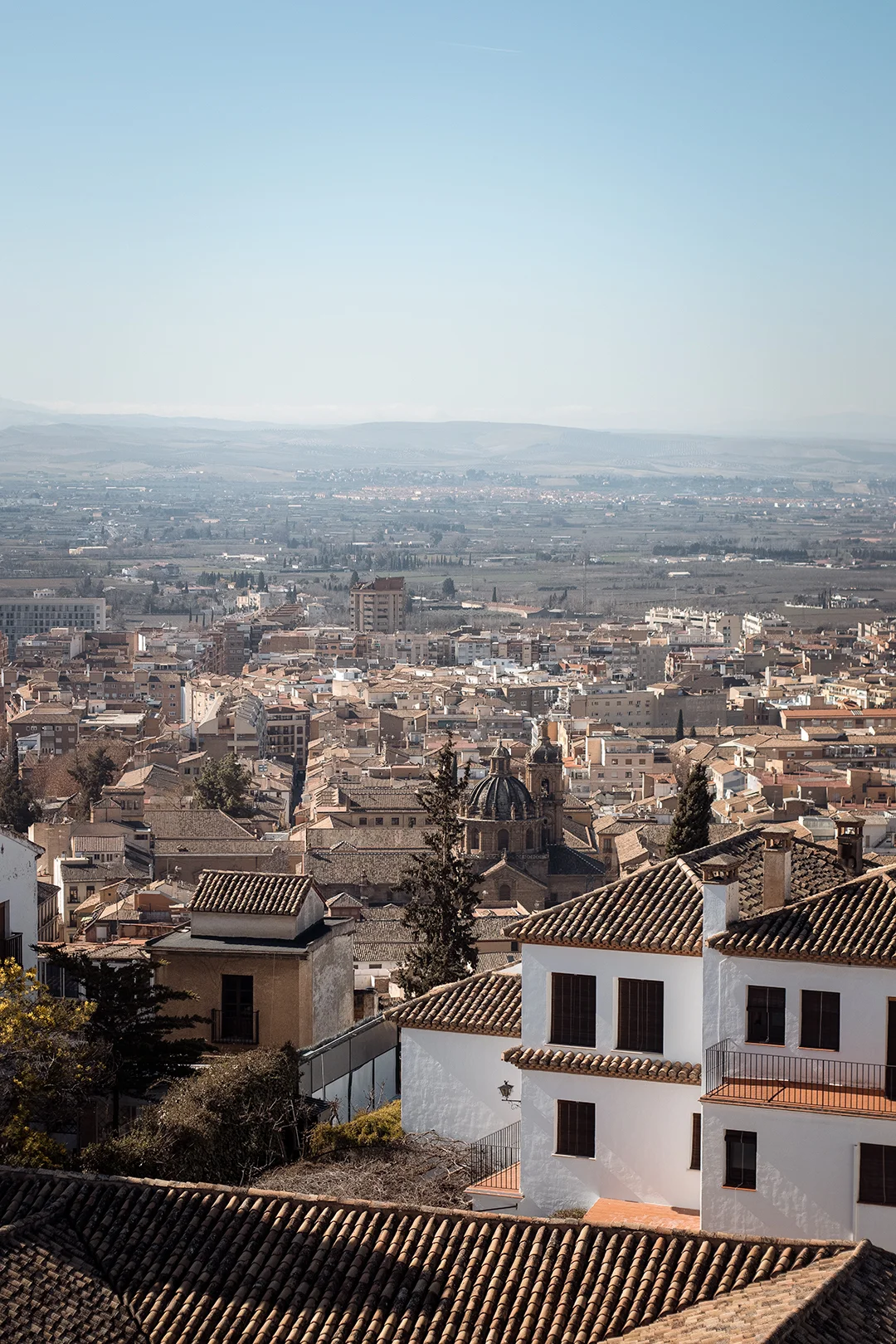 A sweeping panoramic view of Granada from the heights of the Albaicín — terracotta rooftops, the city cathedral dome, and the vast Vega de Granada stretching to the horizon. A sweeping panoramic view of Granada from the heights of the Albaicín — terracotta rooftops, the city cathedral dome, and the vast Vega de Granada stretching to the horizon.